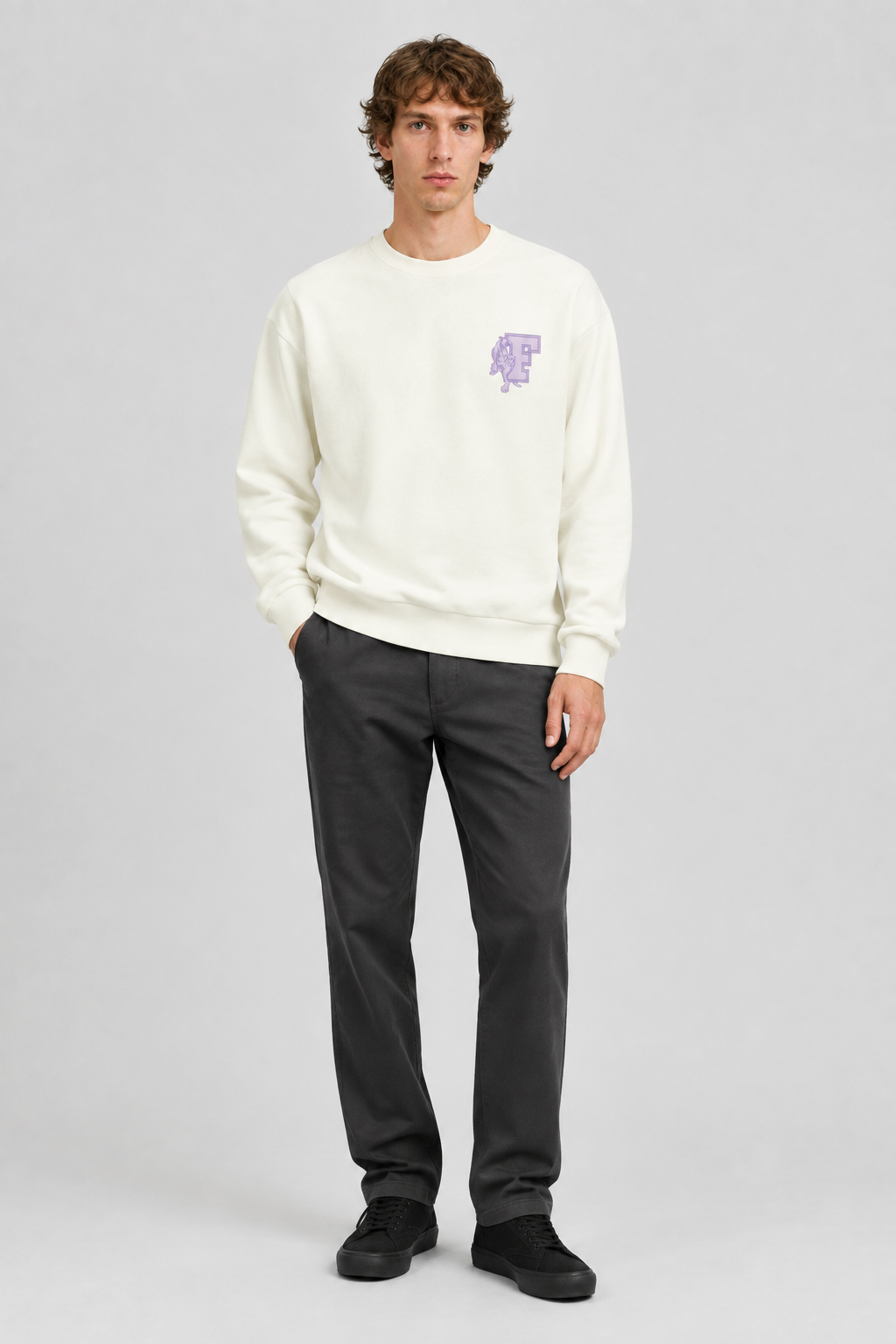 Mannelijk model met de crèmekleurige Dan Fox Apparel Sweater Jesper met paars borstmotief, volledig van voren gefotografeerd
